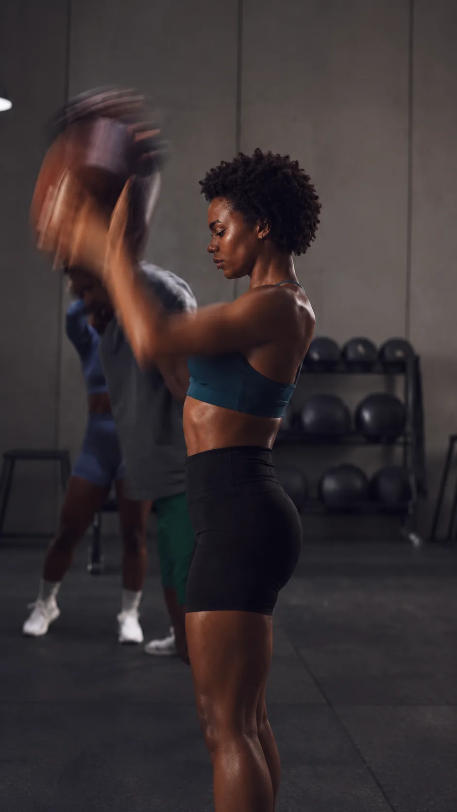 A woman swinging a medicine ball while a friend trains behind her